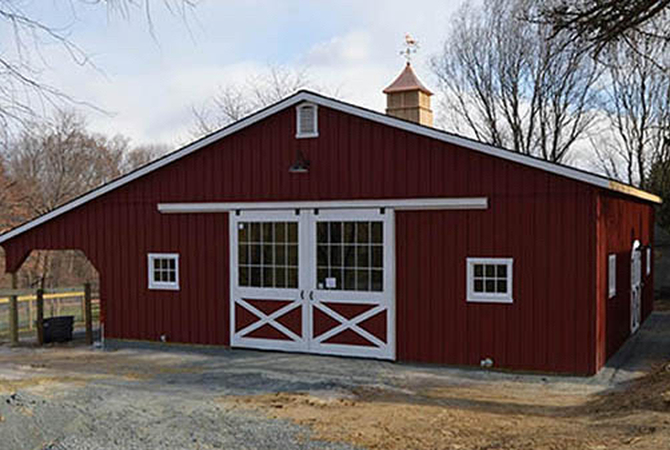 A small red center-aisle horse barn by Horizon Structures.
