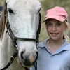 Young girl in pink baseball cap with her white horse.