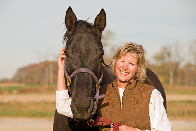 Smiling woman enjoying caring for a horse on a sunny day.
