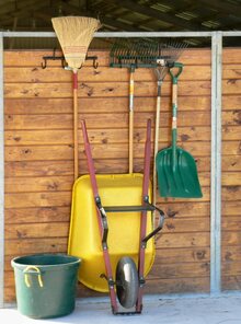 Organized tools including muck rake and broom on a stable wall.