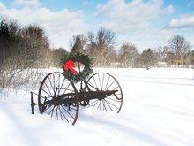 A festive wreath with a red ribbon welcomes holiday visitors to a snow-covered farm.