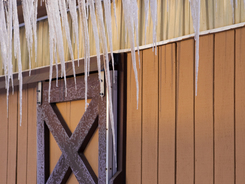 Winter barn with icicles and snow above a closed window