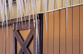 Winter barn with icicles and snow above a closed window
