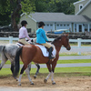 Two riders wearing helmets and returning to the horse barn after a ride.