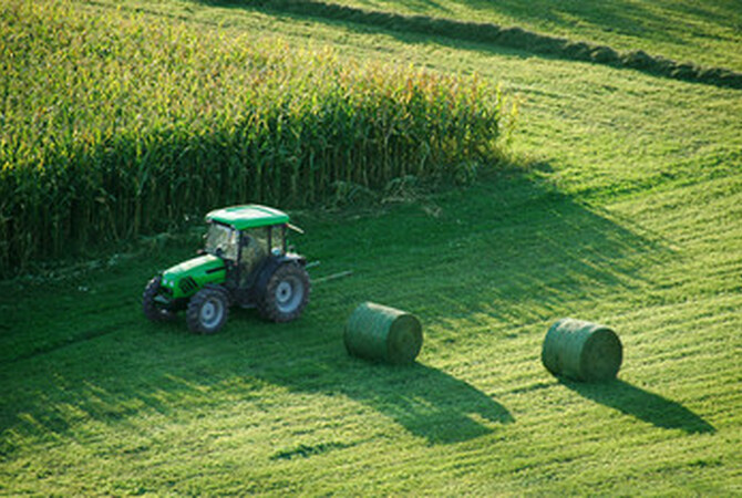 Harvesting hay with tractor and equipment making it into large, round bales.