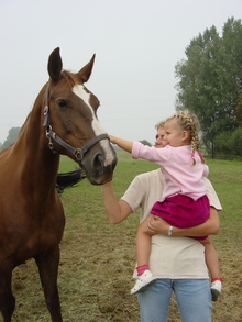 Little girl and Mom petting horse in pasture.