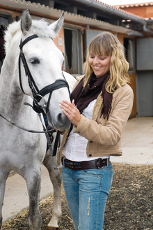 Young woman happily caring for her white horse.