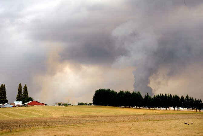 Country flat-land setting with wild fire plumes of smoke approaching.