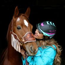 Woman wearing a helmet cozying up to her horse.